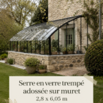 Serre en verre trempé élégamment intégrée dans un jardin bien entretenu.